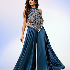 Puede incluir: Un conjunto de dos piezas en color turquesa con pantalón de pernera ancha y top halter. El top tiene un estampado de cachemira en tonos azules, dorados y marrones. El pantalón es de color turquesa liso, con un diseño elegante y fluido.