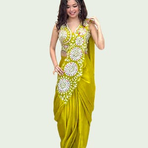 May include: A chartreuse sari with detailed embroidery. The sleeveless top has a V-neck, and the skirt is draped. The embroidery features white, pink, and green floral patterns. This traditional garment is a vibrant example of Indian fashion.