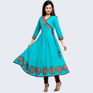 May include: A turquoise wrap dress with long sleeves and a flared skirt. The dress has red trim and embroidered circular patterns. A matching red tie and maroon leggings complete the outfit.