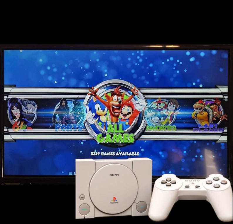 May include: A white Sony PlayStation console and controller are in front of a screen displaying a video game menu. The screen shows the words "ALL GAMES" with various game characters and the text "5319 GAMES AVAILABLE".