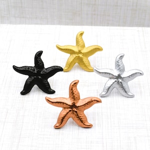May include: Four starfish decorations in metallic finishes: black, gold, silver, and copper. Each starfish has five points and a textured surface. These decorative accents are suitable for coastal or nautical-themed decor.