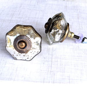 May include: Two decorative cabinet knobs with a vintage aesthetic. The knobs have a multifaceted, silver-toned glass design with brass and bronze accents. One knob is shown from the front, the other from the side, with the screw and hardware visible.