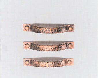 May include: Three copper-colored cabinet pulls with a hammered texture. Each pull has a curved handle and is secured with hexagonal bolts at each end. The pulls are arranged vertically against a white background.