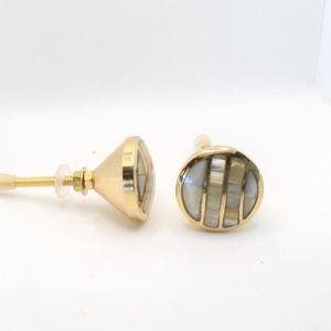 May include: Two decorative cabinet knobs with a gold finish. The knobs have a round, inlaid design with a mother-of-pearl appearance. One knob is round, and the other is cone-shaped. Each knob has a screw for installation.