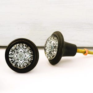 May include: A set of three ceramic mugs with a speckled, cream-colored glaze. Each mug features a different hand-painted design: a blue and green leaf, a yellow flower, and a red berry. The mugs have a simple, rounded shape.