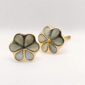 May include: Two flower-shaped cabinet knobs. Each knob features a gold-colored metal frame with a floral design. The petals are filled with a pearlescent, light gray material. The knobs are designed for furniture and home decor.