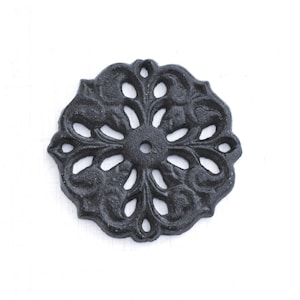 May include: A black, cast iron decorative rosette with an ornate floral design. The circular piece features openwork detailing and a central hole. This decorative element is suitable for furniture or craft projects.