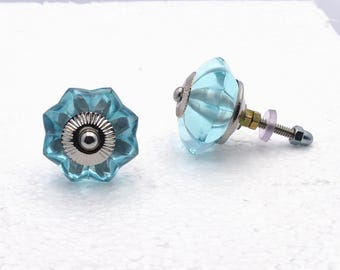 May include: Two light blue glass cabinet knobs with a starburst design. The knobs have a silver metal base and a screw with a nut for installation. The glass has a faceted, jewel-like appearance, adding a decorative touch to furniture.