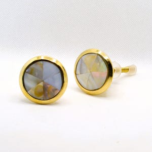 May include: Two round earrings with a gold-colored border. The center of each earring features a multi-colored, iridescent design. One earring has a post for insertion. The earrings are set against a white background.