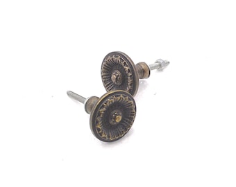 May include: Two antique bronze cabinet knobs with a detailed, circular design. Each knob has a central raised circle surrounded by a textured pattern. The knobs are attached to silver-colored screws, ready for installation. The hardware has a vintage aesthetic.