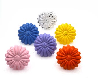 May include: A collection of six daisy-shaped cabinet knobs in various colors. The knobs are painted in shades of pink, blue, purple, yellow, and orange, with a distressed white knob. These decorative knobs are ideal for adding a pop of color to furniture.