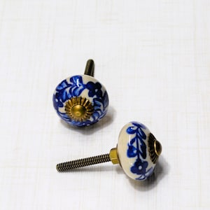 May include: Two ceramic cabinet knobs with a floral design in blue and white. The knobs have a brass-colored base and a threaded metal screw for installation. The knobs are round and have a glossy finish.