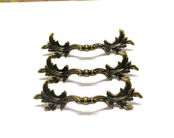 May include: Three antique bronze drawer pulls with ornate, symmetrical leaf and scroll designs. The hardware is arranged in a horizontal stack, showcasing the decorative details and aged finish. The pulls are set against a white background.