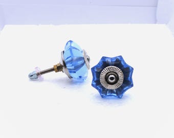 May include: Two blue glass cabinet knobs with a faceted design. The knobs have a silver-colored metal base and a threaded post with a nut and washer for installation. The knobs are a light blue color and have a starburst shape.