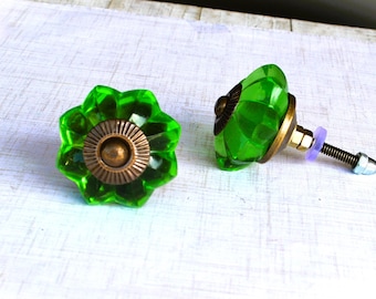 May include: Two decorative cabinet knobs. The knobs feature a faceted, flower-shaped design in a vibrant green color. The base is a bronze color, and the hardware includes a screw and nut for installation.