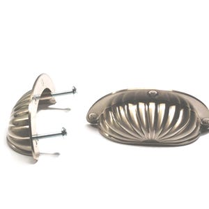 May include: Two brushed nickel-finished shell-shaped drawer pulls with mounting screws. The pulls have a fluted design and are set against a white background. The hardware is designed for cabinets and drawers.