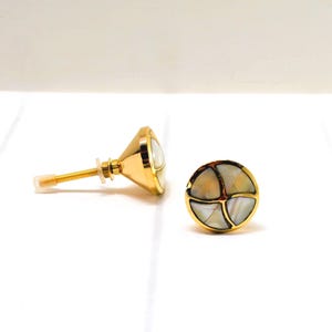 May include: Two gold-colored cabinet knobs with a mother-of-pearl inlay. One knob is lying on its side, showing the screw and washer. The other knob is upright, displaying the circular design with a gold border.