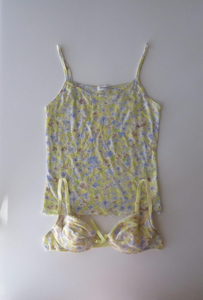 May include: A yellow camisole with thin straps and a blue and white floral pattern paired with a matching underwire bra featuring the same floral print, a small yellow center bow, and adjustable shoulder straps on a plain white background.