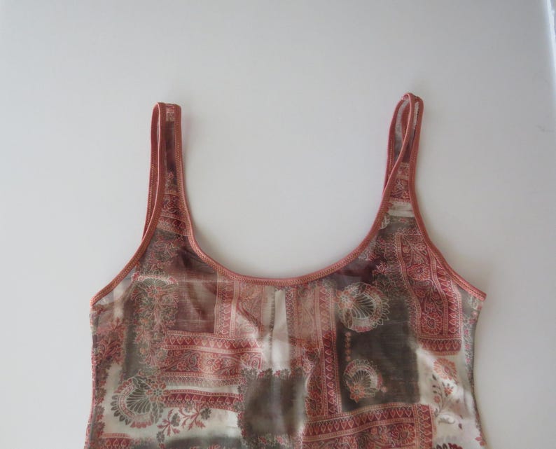 May include: A sleeveless tank top featuring a scoop neckline and thin shoulder straps. The garment is made of a semi-sheer fabric with a multi-colored patchwork pattern in shades of terracotta, brown, and cream, including floral and geometric motifs.
