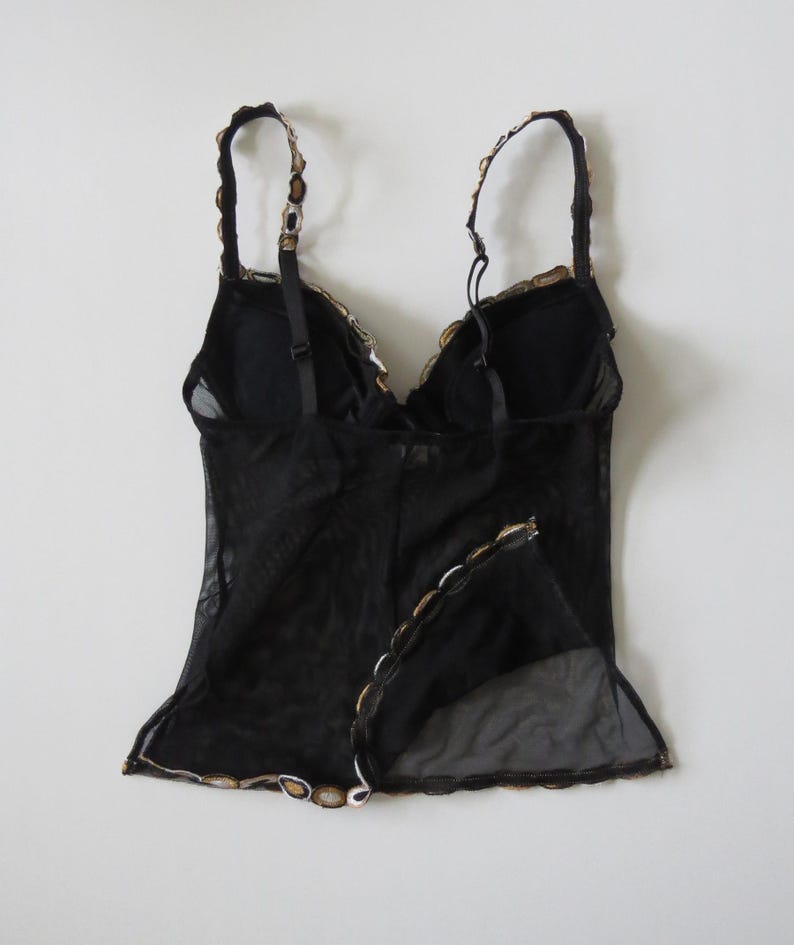 Puede incluir: Top de lencer&iacute;a negro con tirantes ajustables y un dise&ntilde;o de malla transparente. El top presenta un ribete festoneado con detalles dorados y blancos a lo largo del escote y el dobladillo. La espalda tiene un cierre de corchete y ojal.