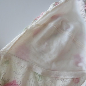 Pu&ograve; includere: Un bralette a triangolo bianco caratterizzato da un delicato motivo floreale con rose rosa e foglie verdi. Il capo &egrave; realizzato con una fodera in tessuto morbido e rifinito con un bordo in pizzo smerlato lungo i lati e spalline sottili.