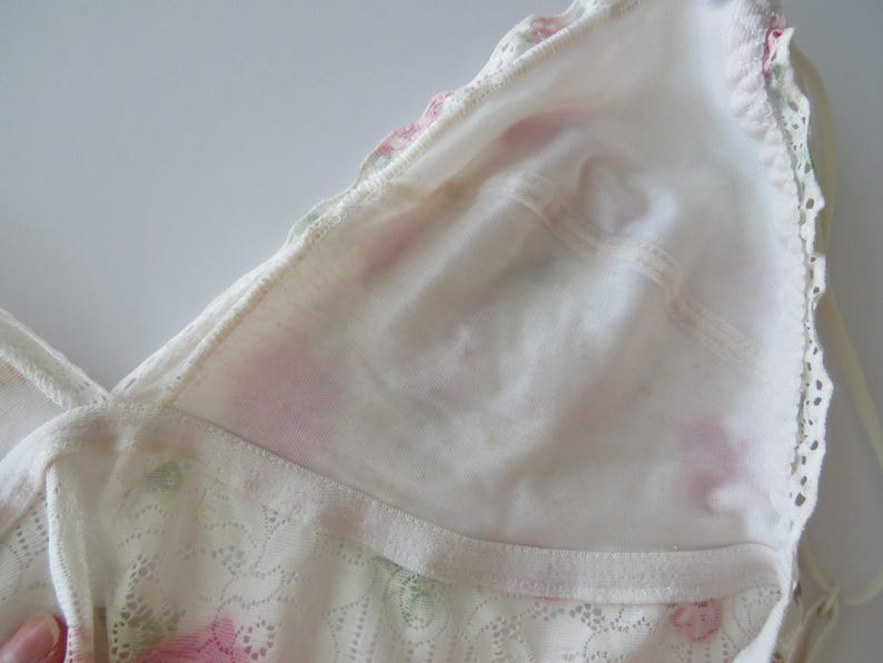 Pu&ograve; includere: Un bralette a triangolo bianco caratterizzato da un delicato motivo floreale con rose rosa e foglie verdi. Il capo &egrave; realizzato con una fodera in tessuto morbido e rifinito con un bordo in pizzo smerlato lungo i lati e spalline sottili.