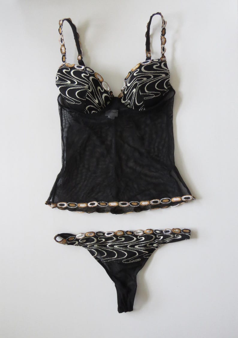 Puede incluir: Conjunto de lencer&iacute;a negra con top transparente y tanga a juego. El conjunto est&aacute; adornado con intrincados bordados en tonos dorados y plateados, creando un patr&oacute;n decorativo. Las correas y los bordes est&aacute;n adornados con detalles similares.