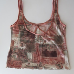 May include: A sleeveless tank top featuring a patchwork-style print in shades of brown, cream, and muted red. The garment has a scoop neckline and a unique back design with crisscrossing straps, finished with a delicate lettuce-edge hemline.