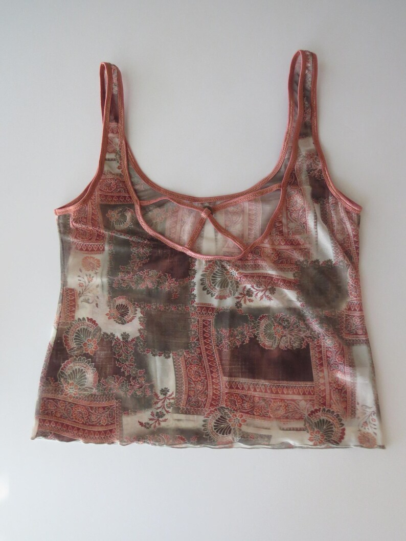 May include: A sleeveless tank top featuring a patchwork-style print in shades of brown, cream, and muted red. The garment has a scoop neckline and a unique back design with crisscrossing straps, finished with a delicate lettuce-edge hemline.