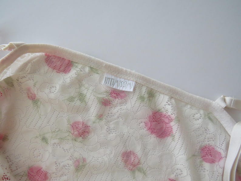 Pu&ograve; includere: Una canotta in pizzo color crema con un delicato motivo floreale di rose rosa e foglie verdi. Il capo presenta sottili spalline regolabili e un'etichetta in tessuto bianco con la scritta Intimissimi cucita nello scollo.
