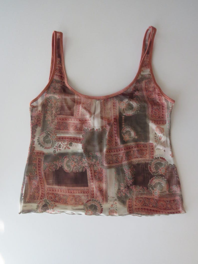 May include: A sleeveless tank top featuring a sheer, lightweight fabric with a multi-colored patchwork print in shades of terracotta, brown, and cream. The garment has a scoop neckline, wide shoulder straps, and a straight hemline with a subtle wavy edge.