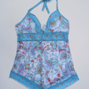 Pu&ograve; includere: Un top tankini azzurro stile allacciato al collo con base bianca e stampa floreale e paisley colorata. Il capo presenta una sezione centrale in rete trasparente, bordi blu tinta unita lungo lo scollo e l'orlo, e spalline regolabili al collo.
