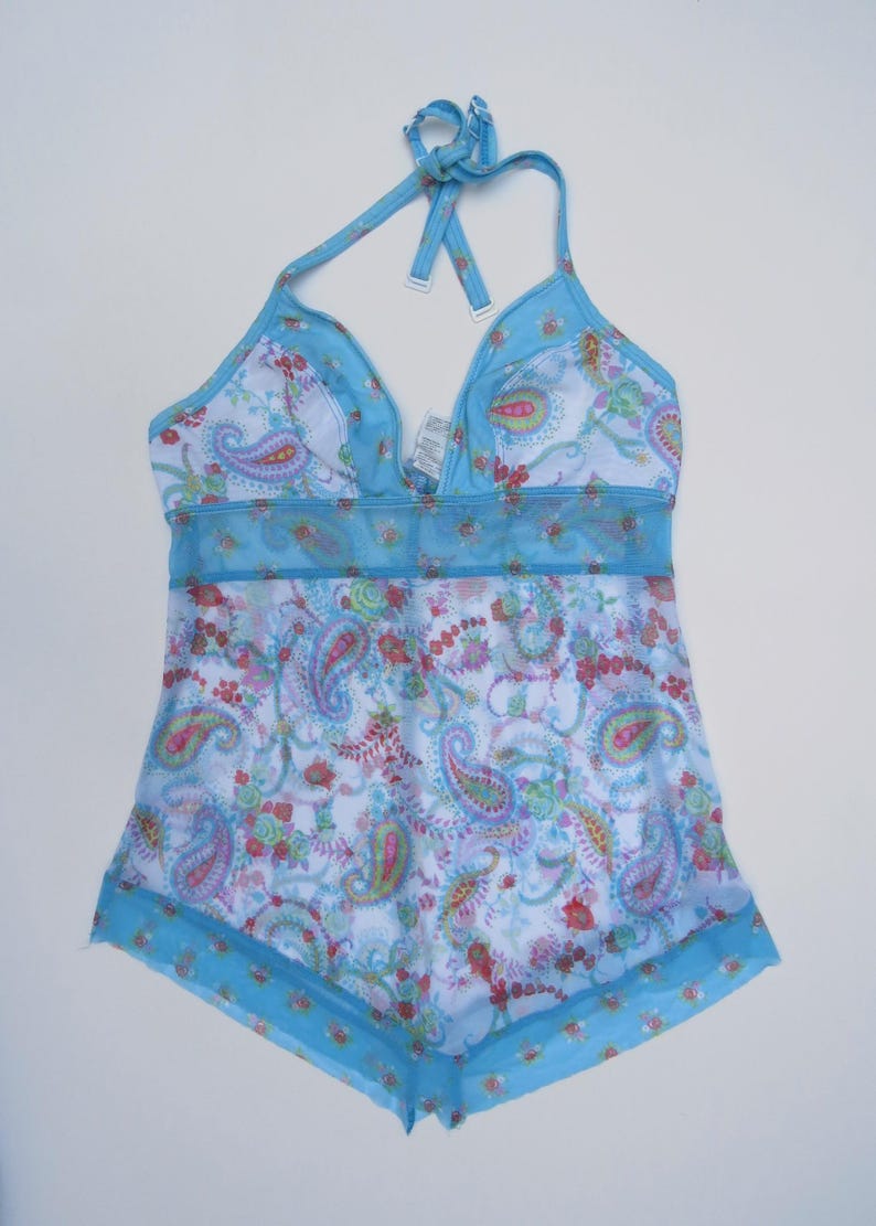 Pu&ograve; includere: Un top tankini azzurro stile allacciato al collo con base bianca e stampa floreale e paisley colorata. Il capo presenta una sezione centrale in rete trasparente, bordi blu tinta unita lungo lo scollo e l'orlo, e spalline regolabili al collo.