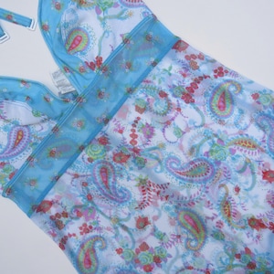 Pu&ograve; includere: Un costume da bagno azzurro in stile allacciato al collo con base bianca e un colorato motivo cachemire e floreale nei toni del rosa, verde e blu. Il capo presenta un pannello in rete trasparente sul petto e spalline regolabili con dettagli bianchi.