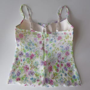 May include: A sleeveless camisole top featuring a delicate floral print with pink, purple, blue, and green flowers on a white background. The garment has thin shoulder straps, a scalloped neckline, and a scalloped hem with a center back zipper.