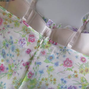 May include: A sleeveless bodice featuring a white base with a colorful floral print in shades of pink, blue, yellow, and green. The garment includes a structured, cream-colored interior lining, adjustable shoulder straps, and a center back zipper.
