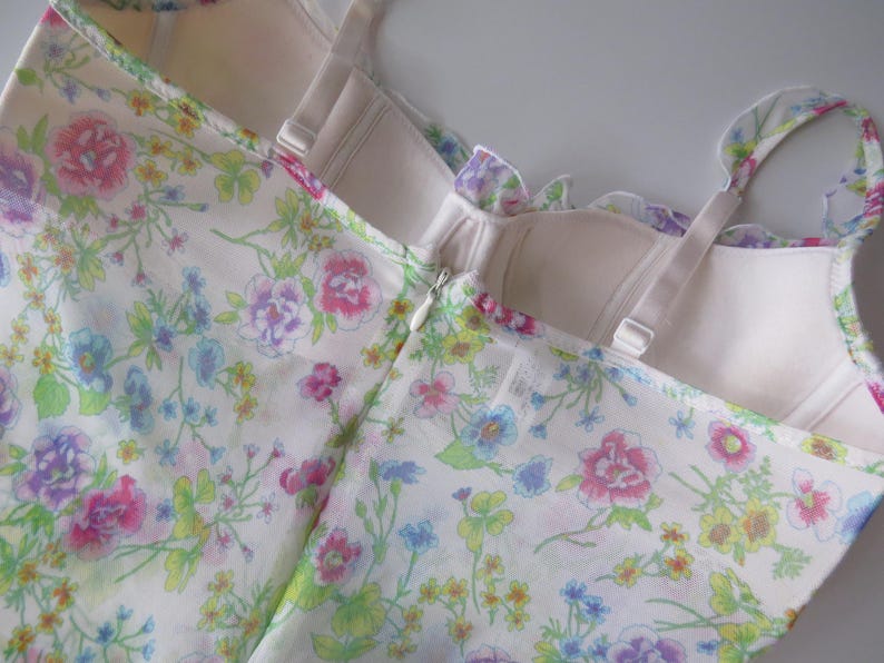 May include: A sleeveless bodice featuring a white base with a colorful floral print in shades of pink, blue, yellow, and green. The garment includes a structured, cream-colored interior lining, adjustable shoulder straps, and a center back zipper.