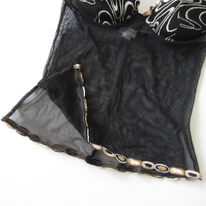 Puede incluir: Una taza de cer&aacute;mica blanca con asa negra y el texto "But First, Coffee" en negrita negra. La taza se encuentra sobre un fondo borroso, sugiriendo un ambiente acogedor.