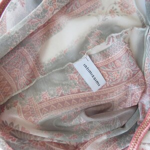 May include: A sheer mesh garment featuring a muted pink, cream, and sage green paisley pattern. The fabric has a fine, semi-transparent texture with a visible white interior tag printed with the brand name intimissimi in black lowercase letters.