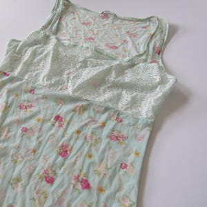 Puede incluir: Camiseta sin mangas con estampado floral azul claro y un panel de encaje blanco en el pecho. La camiseta sin mangas presenta un escote redondo y un estampado floral en rosa y amarillo.