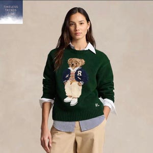 May include: Dark green sweater with a teddy bear design wearing a letterman jacket with the letter "R". The sweater is worn with a white collared shirt and beige trousers. The text "Timeless Trends Wear" is in the upper left corner.