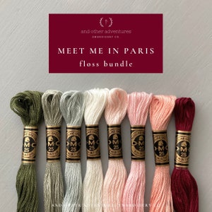 May include: A set of eight DMC embroidery floss spools in various shades of green, gray, beige, pink, and red. The spools are labeled "DMC 25" and "8 m (8.7 yd)". The text "Meet Me in Paris floss bundle" is displayed above the spools.