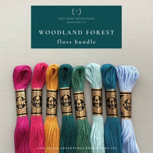 May include: A set of eight embroidery floss spools in various colors, including pink, orange, yellow, green, blue, and light blue. The spools are labeled "DMC" and have the number "25" printed on them. The text "WOODLAND FOREST floss bundle" is printed above the spools.