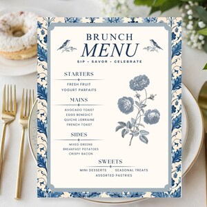 May include: A brunch menu card with a blue and cream floral design. The menu lists starters, mains, sides, and sweets. Gold cutlery and a plate with a donut are in the background.