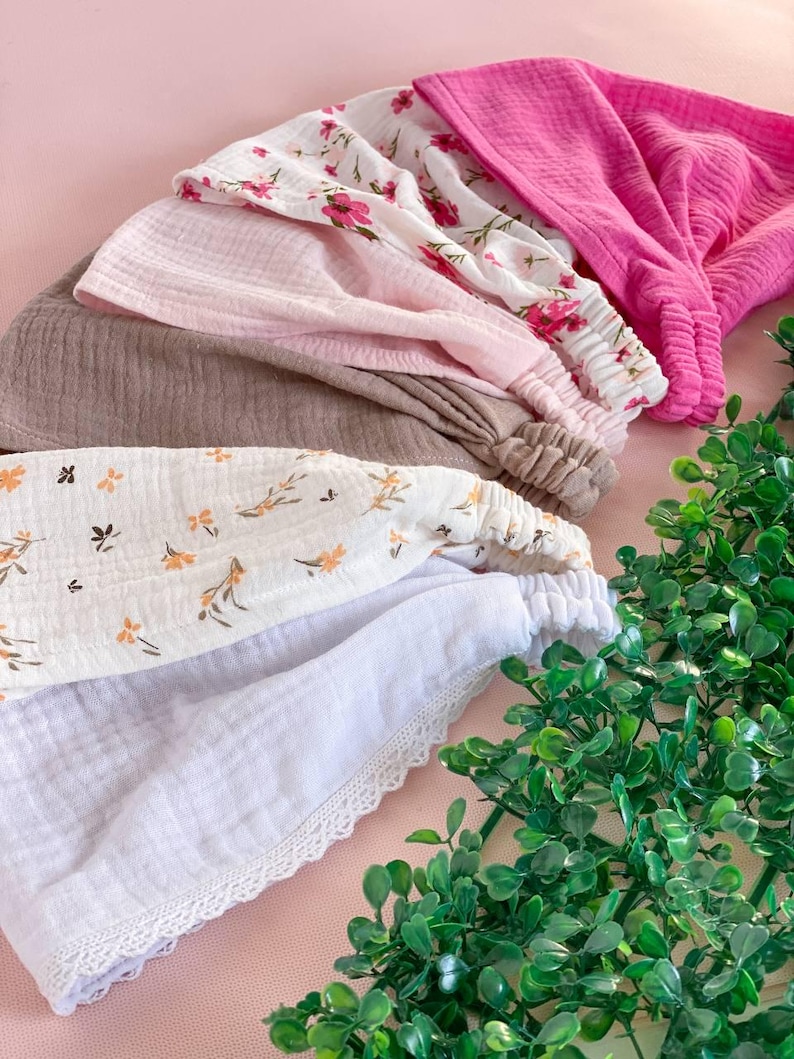 May include: A collection of headbands in various colors and patterns. The headbands include solid pink, floral print, and white with lace trim. The headbands are made of soft fabric and are arranged in a layered display.