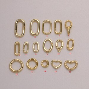May include: A collection of sixteen gold-toned metal jewelry clasps and connectors in various shapes, including oval, circular, and heart designs. Each piece features a spring-loaded gate mechanism, labeled with red numbers from one to sixteen.