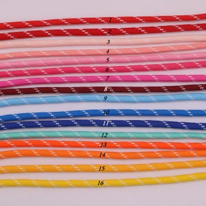May include: Sixteen parallel lengths of braided cord arranged horizontally, each featuring a distinct solid color with a repeating white diagonal dash pattern. The colors range from red, pink, and burgundy to blue, turquoise, orange, and yellow.