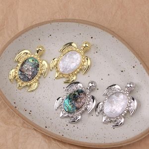 May include: Four turtle-shaped pendants featuring oval centers. Two pendants have gold-toned metal frames with iridescent abalone shell and white mother-of-pearl inlays. Two pendants have silver-toned metal frames with matching abalone and pearl inlays.
