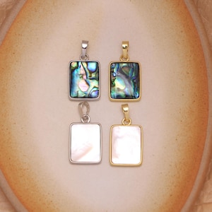 May include: Four rectangular pendants with metal bails. Two pendants feature iridescent abalone shell inlays, one set in silver-tone metal and one in gold-tone metal. Two pendants feature smooth white mother-of-pearl inlays, one in silver and one in gold.