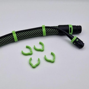 Könnte beinhalten: Ein schwarzes Kabel mit einer grünen, texturierten Ummantelung und schwarzen Anschlüssen, mit zwei am Kabel befestigten grünen Kabelmanagement-Clips sowie vier weiteren losen grünen Clips mit strukturierter Oberfläche zur Kabelorganisation.